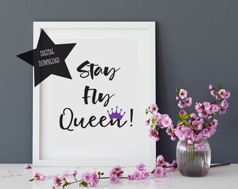 以下が含まれることがあります： 「Stay Fly Queen!」の文字が黒い筆記体で書かれた額入りのプリント、紫色の王冠、そして「Digital Download」と書かれた黒い星。ガラスの花瓶に入ったピンクの花と散らばった花びらが装飾的なアクセントになっています。