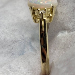 May include: A gold ring with a white opal gemstone and smaller clear gemstones set in the band.