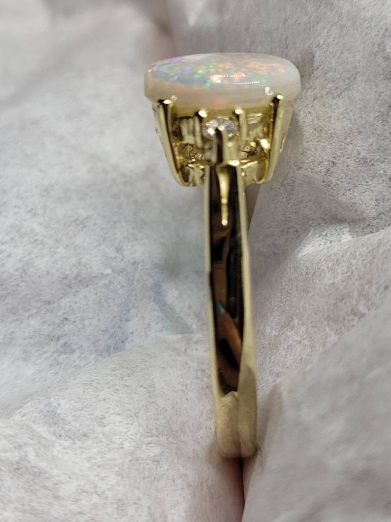 May include: A gold ring with a white opal gemstone and smaller clear gemstones set in the band.