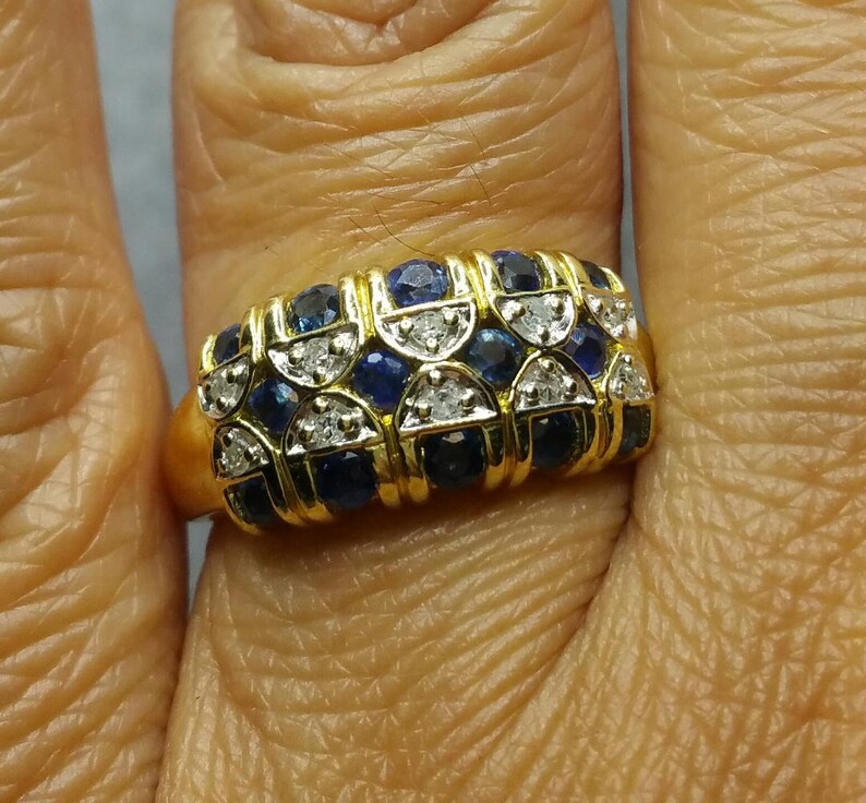 May include: A gold ring with a band of alternating blue sapphires and diamonds. The ring is set in a gold band and has a polished finish.