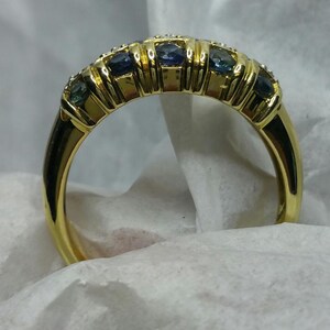 May include: A gold band ring with a row of blue and white gemstones.