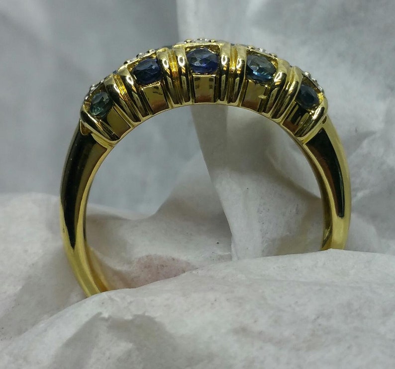 May include: A gold band ring with a row of blue and white gemstones.
