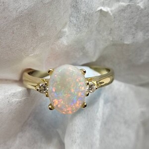 May include: A gold ring with an oval-shaped opal gemstone and two smaller diamond accents.