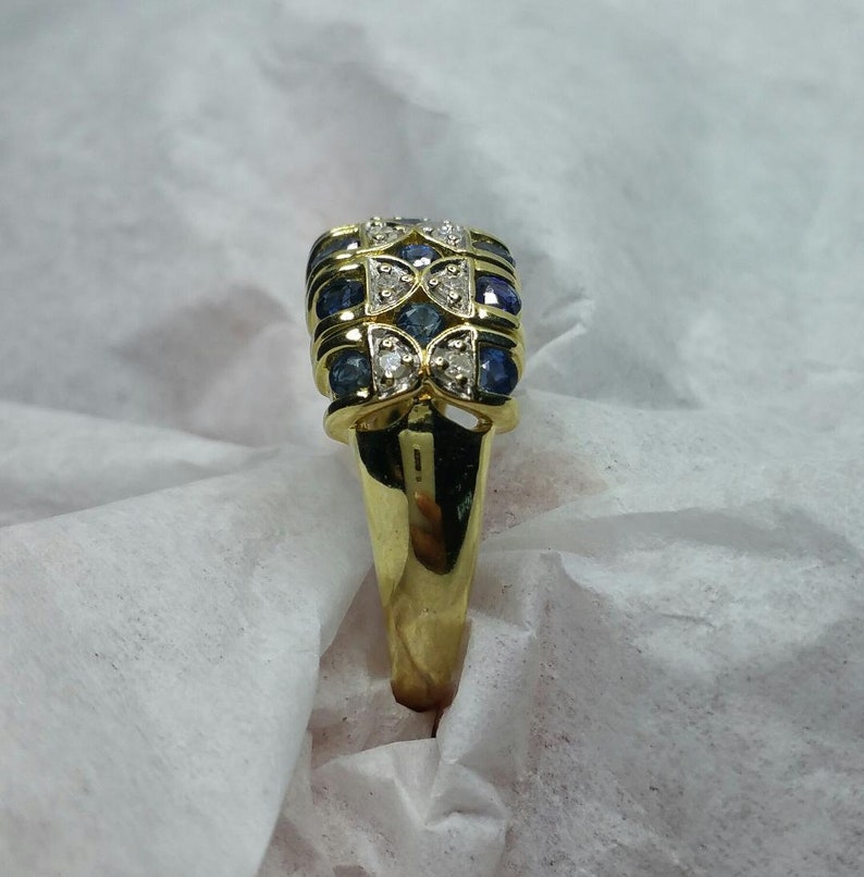 May include: A gold ring with a rectangular setting featuring alternating blue sapphires and white diamonds.