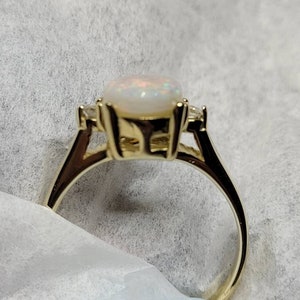 May include: A gold ring with a white opal gemstone and two smaller diamonds on the band.
