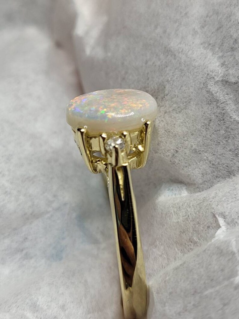 May include: A gold ring with a white opal gemstone and a small diamond accent. The ring has a delicate, ornate design.