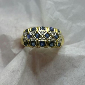May include: A gold ring with a band of blue and white gemstones. The ring is set with a row of blue sapphires and a row of white diamonds.