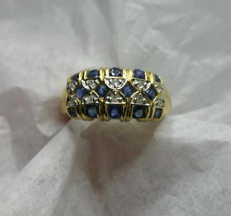 May include: A gold ring with a band of blue and white gemstones. The ring is set with a row of blue sapphires and a row of white diamonds.