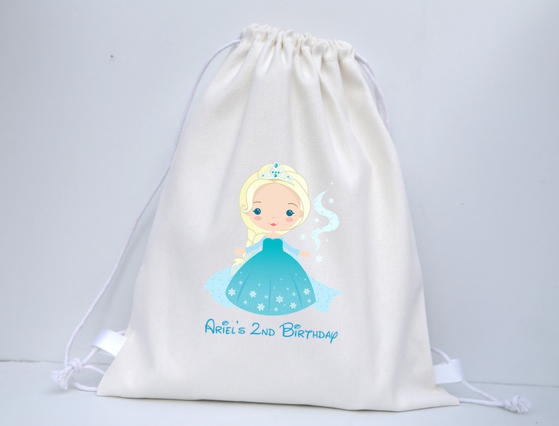 May include: White cotton drawstring bag featuring a printed image of a cartoon princess in a blue dress and crown. The text "Ariel's 2nd Birthday" is printed below the image.