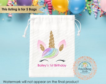 May include: White drawstring bag with a unicorn design featuring a gold horn, pink ears, and rainbow mane. The text "Bailey's 1st Birthday" is printed in pink below the unicorn. The bag is surrounded by confetti and balloons.