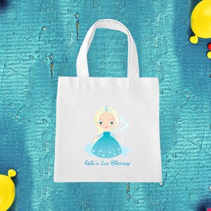 May include: White tote bag featuring a blue and white illustration of a princess with blonde hair and a crown. The text "Ariel's 2nd Birthday" is printed below the illustration.