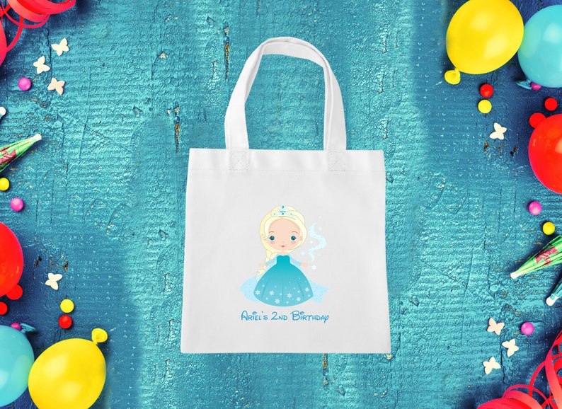 May include: White tote bag featuring a blue and white illustration of a princess with blonde hair and a crown. The text "Ariel's 2nd Birthday" is printed below the illustration.