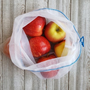 Peut inclure: Un sac en filet blanc pour les produits avec un cordon de serrage bleu, rempli de cinq pommes rouges et jaunes.
