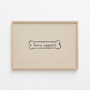 May include: A framed print with a dog bone illustration and the words "bone appétit" in a handwritten style. The artwork is set against a beige background and framed in a light wood frame.