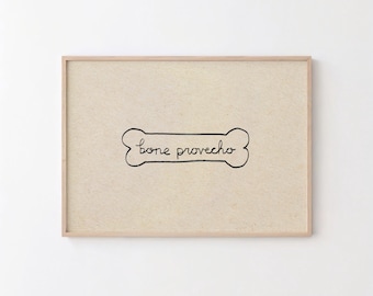 May include: A rectangular wall art print in a light wooden frame featuring a beige textured background. Centered on the print is a black hand-drawn outline of a dog bone shape containing the handwritten black text bone provecho.