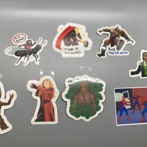 May include: A set of nine stickers featuring various characters and designs from popular movies and TV shows. The stickers include a green Groot, a red-haired woman, a green tree, a black ant, a man in a red cape, a man in a black suit, a man in a green suit, and two Spiderman characters.