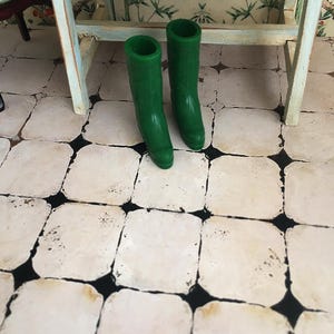 以下が含まれることがあります： 緑色のゴム製のレインブーツのペア。ブーツはタイル張りの床の上に置かれています。