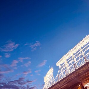 Pode incluir: Uma grande estrutura de metal branco com luzes contra um céu azul com nuvens. A estrutura é um estádio de beisebol.