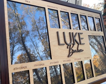 Può includere: Una cornice per foto in legno con sfondo marrone chiaro e bordi neri. La cornice ha 12 spazi per foto, etichettati con i livelli di grado dalla scuola materna alla 12a elementare. La cornice ha anche il nome "LUKE Baha" scritto in lettere nere. La cornice è progettata per contenere foto degli anni scolastici di un bambino.