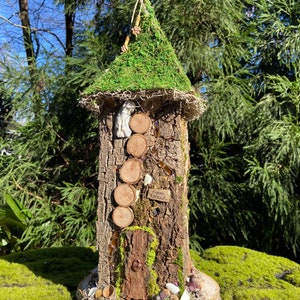 May include: A miniature fairy house made of wood and moss with a green moss roof, a small wooden door, and a sign that reads "Garden Cottage".