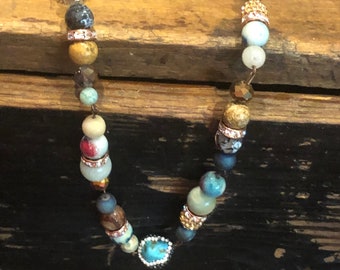 May include: A multi-colored beaded necklace with turquoise, gold, white, and brown beads. The necklace is on a wooden surface.