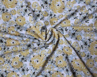May include: A fabric with a repeating floral pattern. The design features yellow roses with black and light blue accents on a white background. The fabric is textured and appears to be folded.