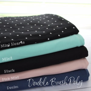 May include: A stack of five fabric swatches in different colors, including black, mint, pink, denim, and a black fabric with white mini hearts. The fabric is labeled "Double Brush Poly".