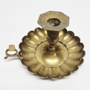 Peut inclure: Un bougeoir en laiton vintage avec une base festonnée et un dessus octogonal. Le support a une petite poignée sur le côté. Le laiton a une patine chaude et vieillie, suggérant qu'il s'agit d'une pièce ancienne ou vintage. Le design est orné et décoratif.