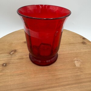 Könnte beinhalten: Eine leuchtend rote Glasvase mit ausgestelltem Rand und rundem Boden. Die Vase hat eine strukturierte Oberfläche und besteht wahrscheinlich aus dickem Glas. Die rote Farbe ist durchgehend, was ihr ein kühnes Aussehen verleiht.