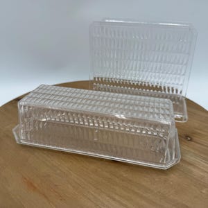 Könnte beinhalten: Zwei transparente Butterdosen aus Kunststoff mit einem Diamantenmuster. Die Dosen sind aus klarem Kunststoff und haben ein Diamantenmuster auf der Außenseite.