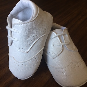 K&ouml;nnte beinhalten: Ein Paar wei&szlig;e Lederschuhe f&uuml;r Babys mit Schn&uuml;rung und Brogue-Muster.