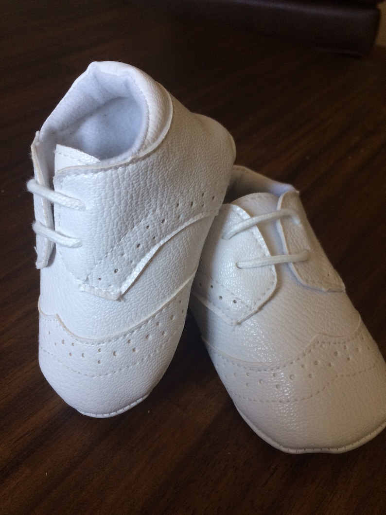 K&ouml;nnte beinhalten: Ein Paar wei&szlig;e Lederschuhe f&uuml;r Babys mit Schn&uuml;rung und Brogue-Muster.