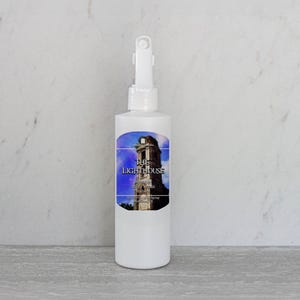 May include: White spray bottle with a white label featuring a blue and white image of a lighthouse with the text "The Lighthouse" on it.