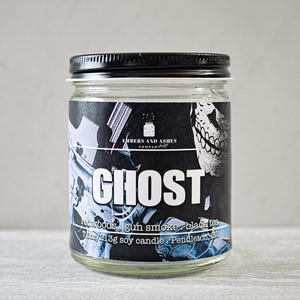 May include: A black glass candle jar with a black lid. The label reads "Embers and Ashes Company" and "Ghost, redwood's gun smoke black tea 7oz/213g soy candle Pendleton, OR".