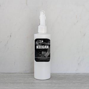 May include: White spray bottle with a black and white label that reads "KEEGAN" and "gun smoke spores". The bottle has a white trigger sprayer and is set against a white and gray background.