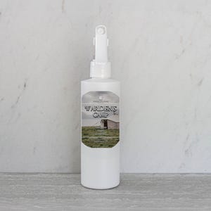 May include: White plastic bottle with a spray nozzle. The bottle label has a green, brown, and white image of a barn and a field. The label text reads "Warden's Camp".