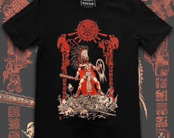 May include: Black t-shirt featuring a red and white illustration of an Aztec warrior holding a club and shield. The warrior stands atop a pile of skulls and weapons, framed by a sun and other Aztec symbols. The shirt has the text "Artangel Expressions" on the top.