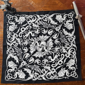 May include: A square black bandana featuring a repeating white line-art pattern of various dragons in flight and coiled positions. The intricate illustration covers the entire fabric surface with detailed wings, scales, and long serpentine tails.