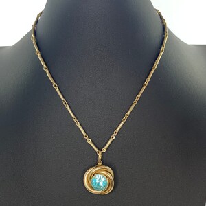 May include: A gold chain necklace with a pendant featuring a blue gemstone set in a gold swirl design.
