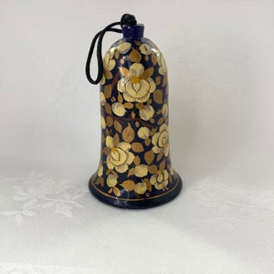 May include: A blue bell ornament with a floral design. The bell is painted with white and gold flowers on a dark blue background.