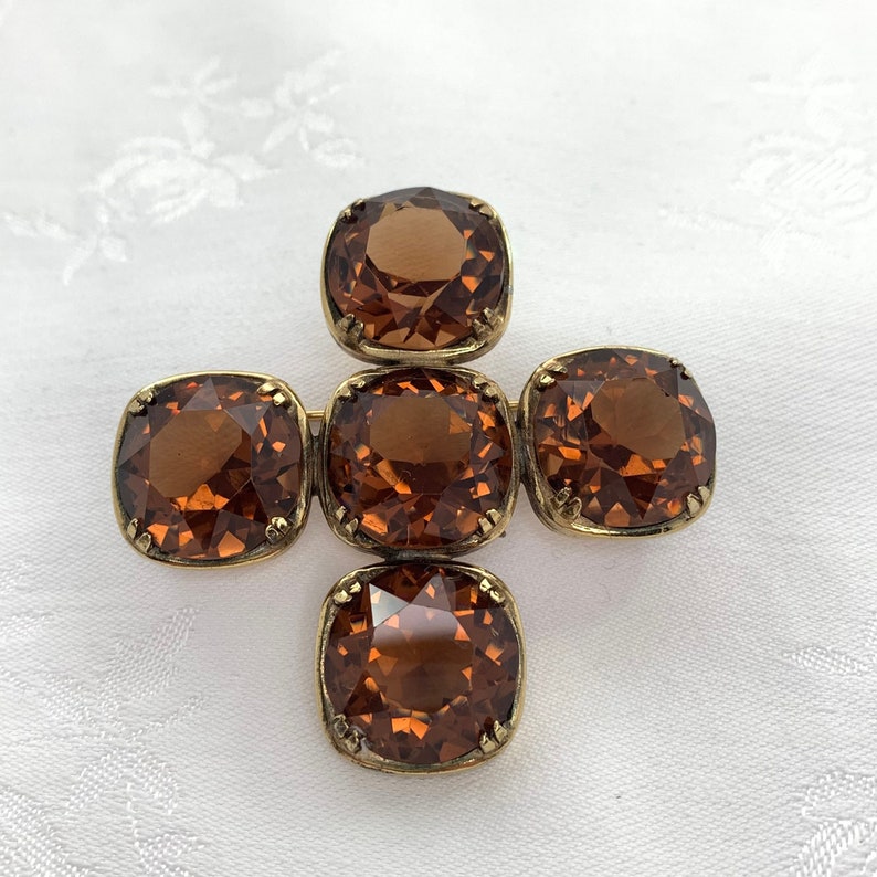 May include: A gold tone brooch with five brown faceted glass stones set in a cross shape.