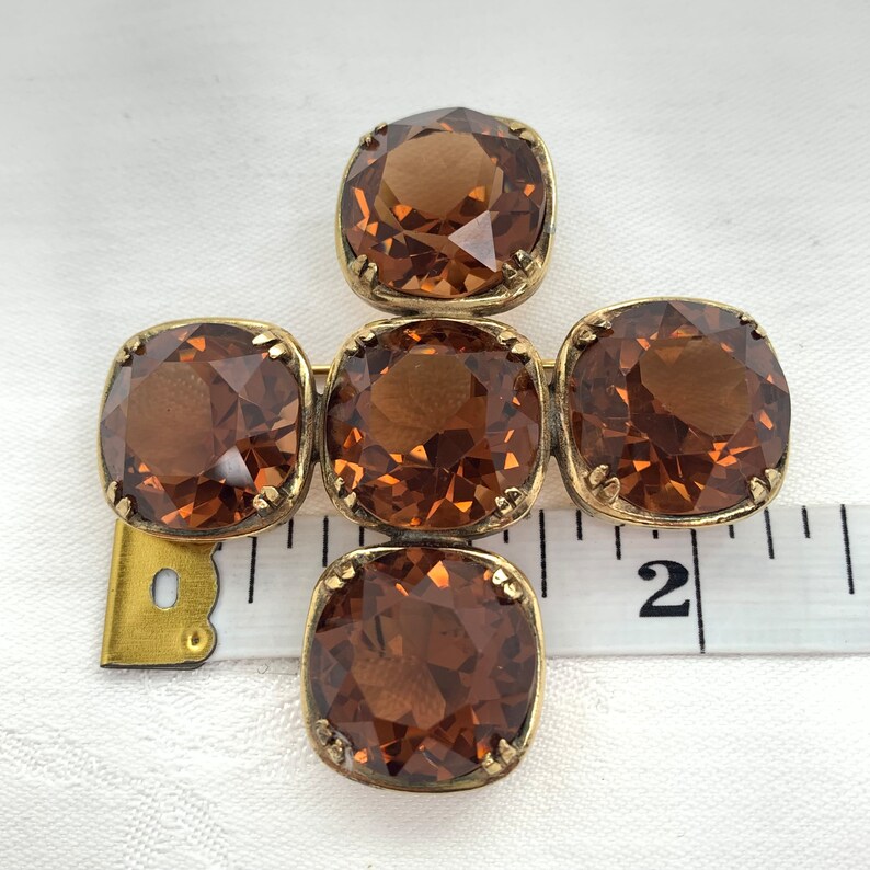 May include: A gold-toned brooch with five brown faceted glass stones arranged in a cross shape.