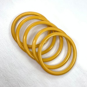 May include: Set of five yellow plastic bangles. The bangles are stacked on top of each other.