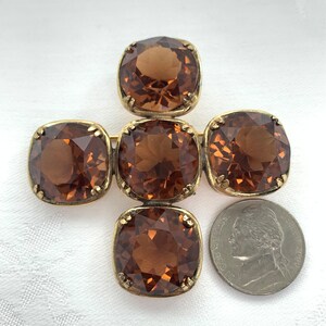 May include: A gold tone brooch with five brown faceted glass stones arranged in a cross shape.