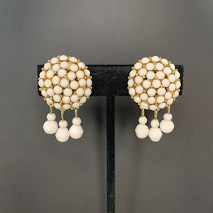 May include: A pair of white and gold earrings with a cluster of white beads on the top and three dangling white beads on each earring.
