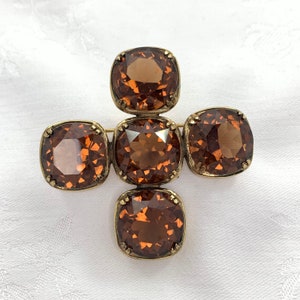 May include: A gold tone brooch with five brown faceted glass stones in a cross shape.
