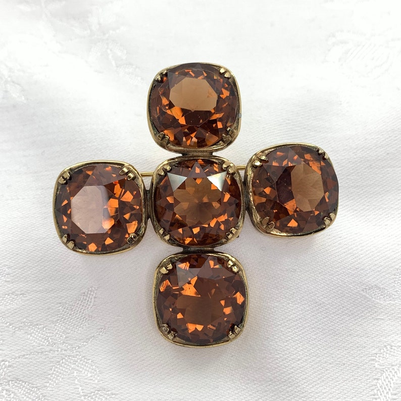 May include: A gold tone brooch with five brown faceted glass stones in a cross shape.