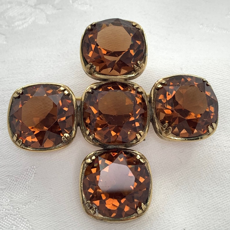 May include: A gold tone brooch with four large, faceted, brown glass stones set in a cross shape.