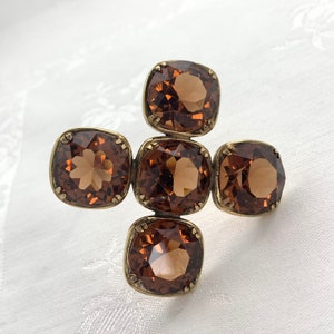May include: A gold-toned cross-shaped brooch with five brown square-shaped rhinestones.