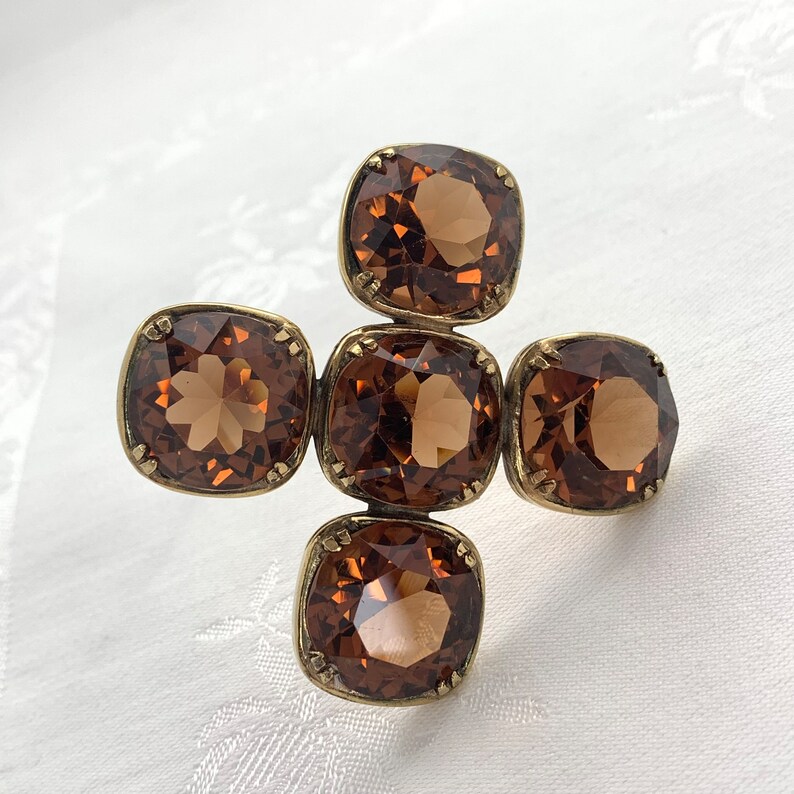 May include: A gold-toned cross-shaped brooch with five brown square-shaped rhinestones.
